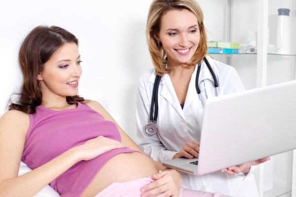 pregnant-young-woman-her-doctor-looking-laptop-indoors